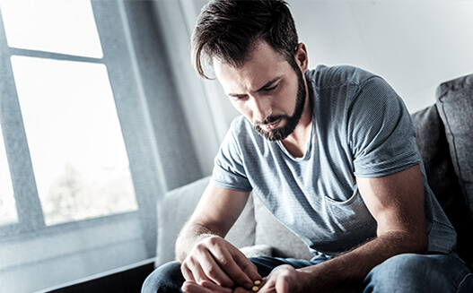 A man sitting on a couch looking at two pills in his hand